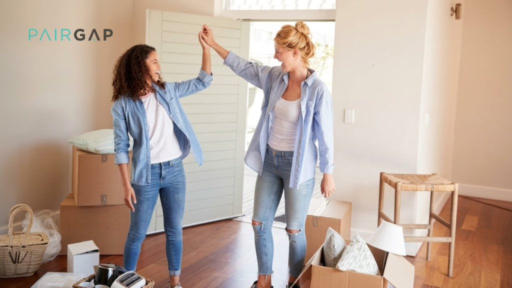Two women celebrating in their new home surrounded by moving boxes, high-fiving after completing a co-buying purchase together.