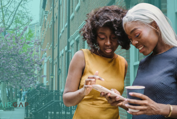 Two women stand on a tree-lined city sidewalk in spring, smiling as they look at a phone together, with the Pairgap logo visible in the lower left corner.