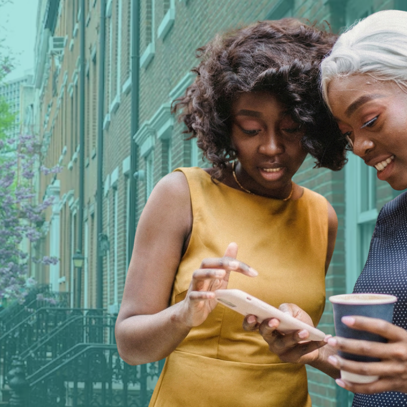 Two women stand on a tree-lined city sidewalk in spring, smiling as they look at a phone together, with the Pairgap logo visible in the lower left corner.
