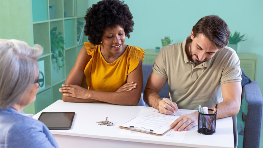 An unmarried couple signing a property agreement with a real estate advisor, house keys visible on the table, representing co-ownership documentation for co-buyers.
