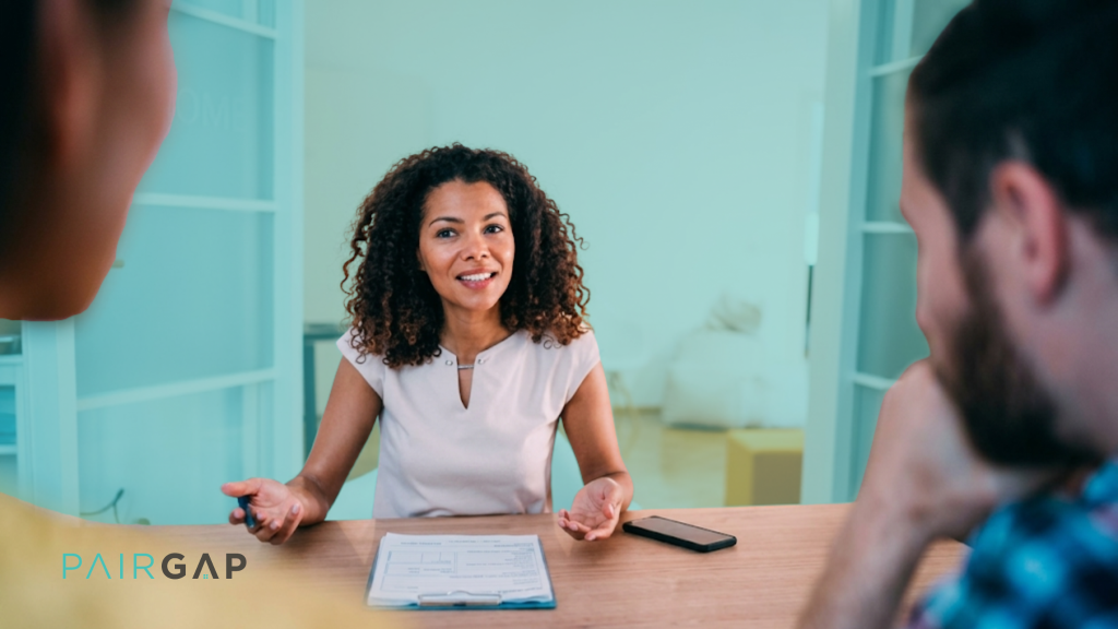 A real estate advisor explaining co-ownership terms to two clients across a table, with a document and the Pairgap logo visible, representing the Real Estate Prenup Builder.