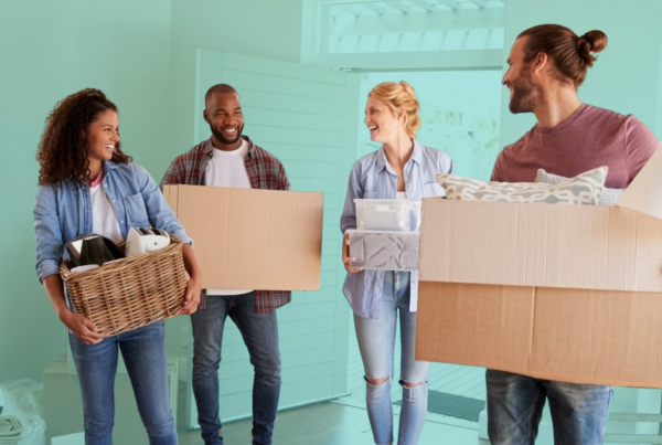 Group of first-time homebuyers carrying moving boxes into a new home, representing shared homeownership and co-buying with friends.