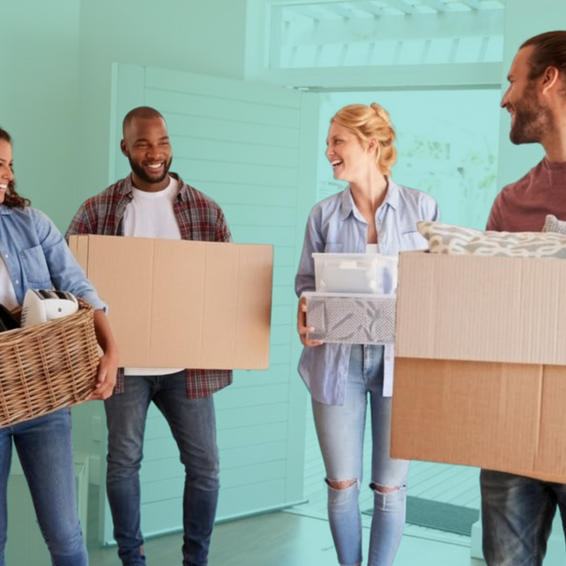 Group of first-time homebuyers carrying moving boxes into a new home, representing shared homeownership and co-buying with friends.