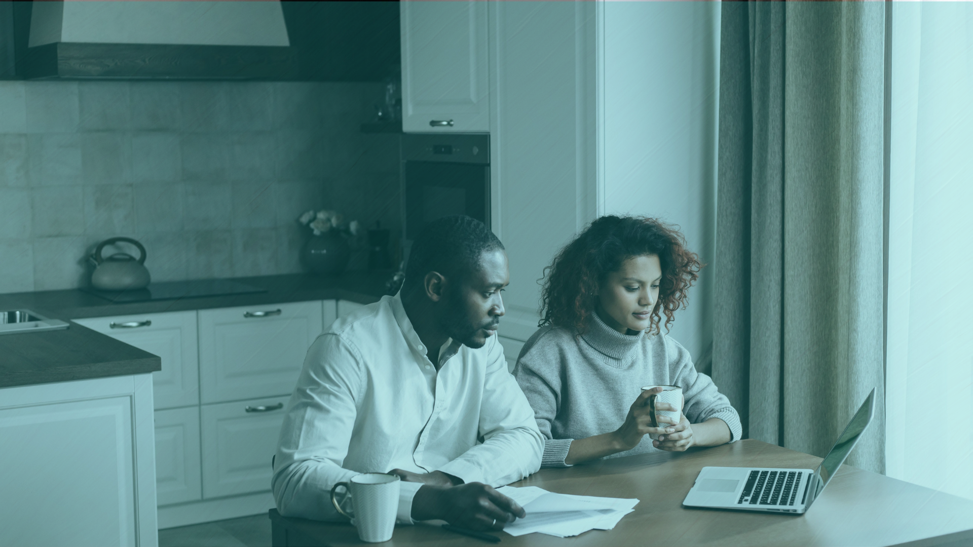 Two co-buyers sitting at a kitchen table reviewing a co-ownership agreement together